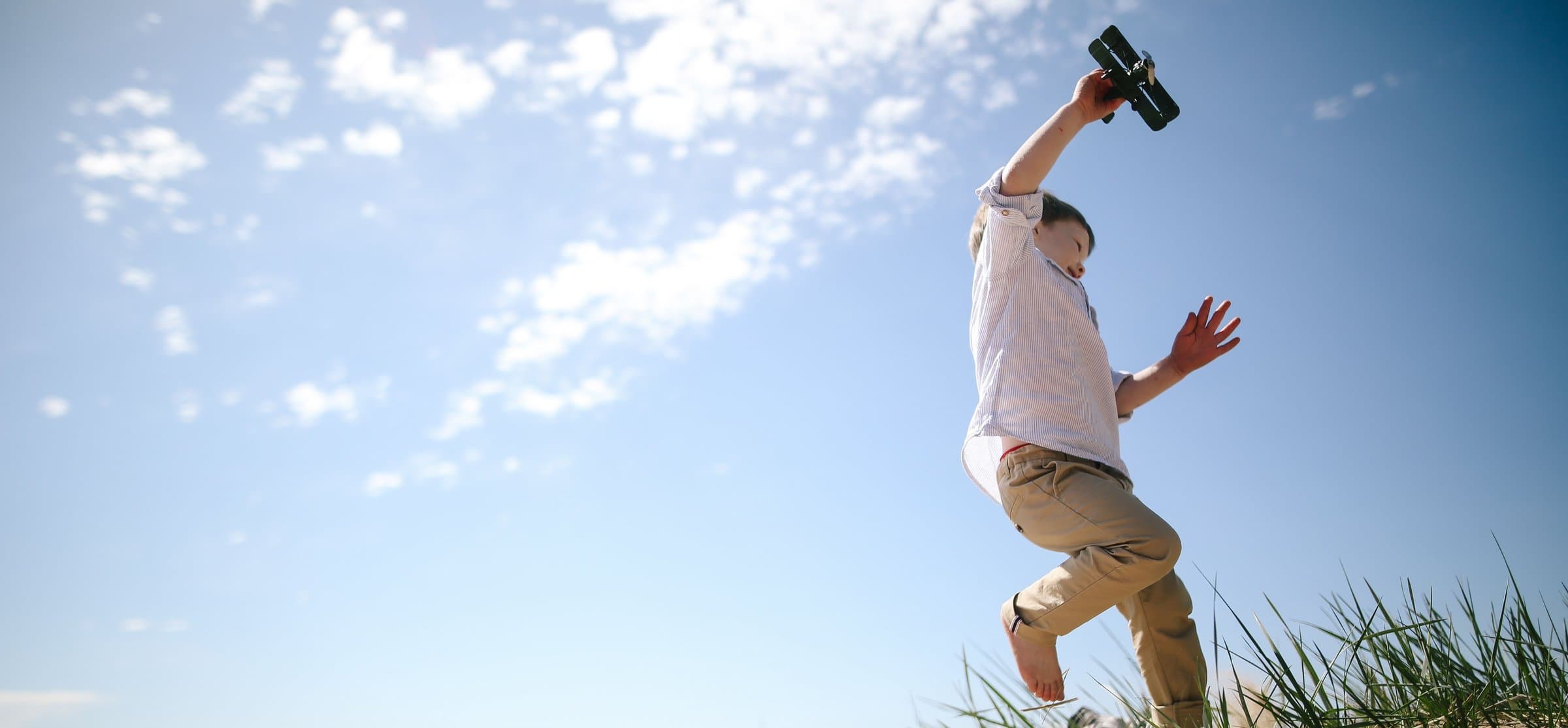 A child leaping down a dune with a toy biplane raised overhead, near Wright by the Beach